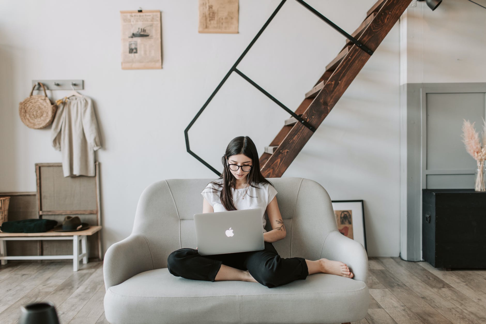 positive young woman using laptop in modern living room with wooden staircase