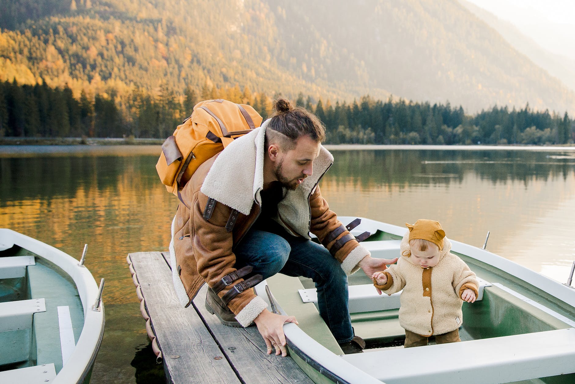 father with little kid standing on boat on wooden pier near lake in mountains